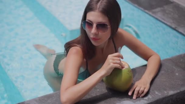 Mujer joven se relaja bebiendo cóctel tropical en una piscina — Vídeo de stock