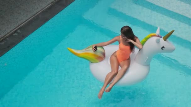 Vrouw fotografeert en drijft op opblaasbare eenhoorn in zwembad — Stockvideo