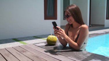 Kadın havuzda dinleniyor, akıllı telefon kullanıyor.