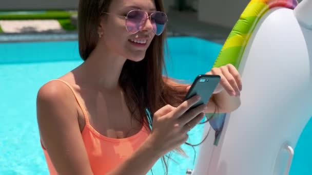 Mulher está vendo redes sociais por smartphone na piscina de verão — Vídeo de Stock