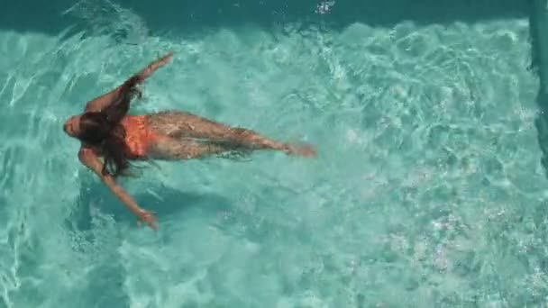 Привлекательная молодая женщина плавает одна в бассейне с кристально чистой голубой водой — стоковое видео