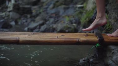 Çıplak ayaklı kadın bambu köprüsünde yürüyor.