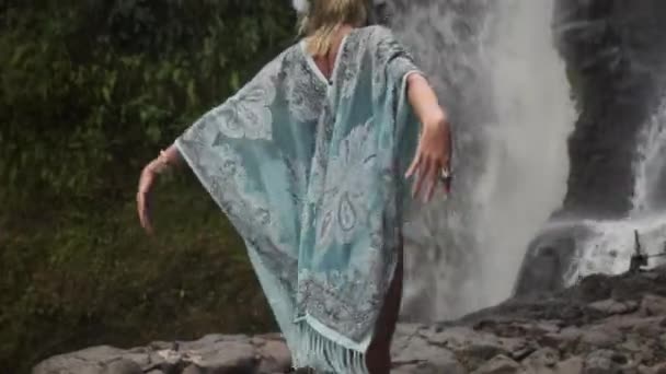 Молода дівчина ідеалізує медитативний танець на скелі поруч з потоком падаючої води — стокове відео