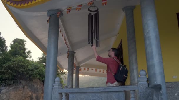Турист звонит в колокол во время прогулки по террасе буддийского храма — стоковое видео