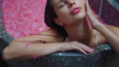 Spa salonundaki kadın, çiçeklerle banyoda dinleniyor, aromaterapi tedavisi görüyor.
