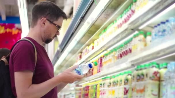 El joven está comprando agua y jugo en el supermercado — Vídeos de Stock
