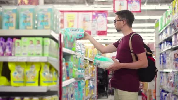 Padre joven está comprando pañales para bebés en el supermercado — Vídeos de Stock