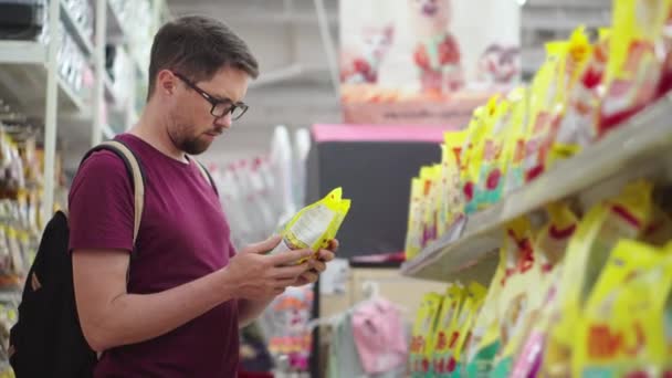 Joven macho está comprando alimentos para mascotas en un hipermercado — Vídeos de Stock