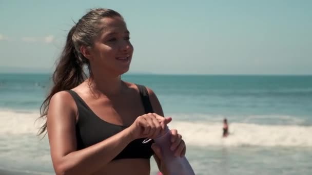 Female runner on beach is resting and sipping water — Stock Video