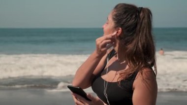 Sporcu kadın okyanusun kumlu sahillerinde müzik dinliyor.