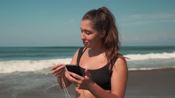 Женщина ставит наушники для прослушивания музыки во время утренней пробежки — стоковое видео