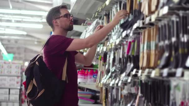 Joven macho está comprando utensilios de cocina en un hipermercado — Vídeos de Stock