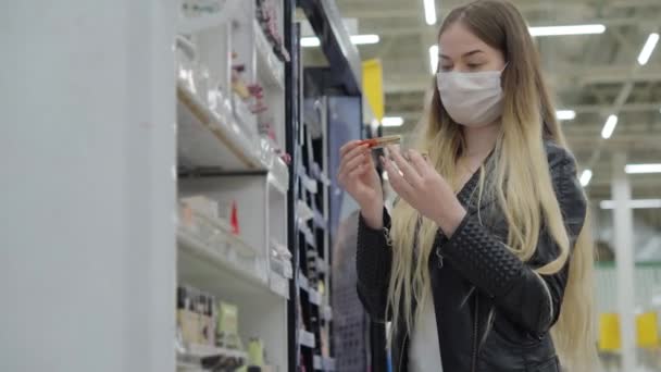 Wanita muda bertopeng medis membeli lip gloss di supermarket — Stok Video