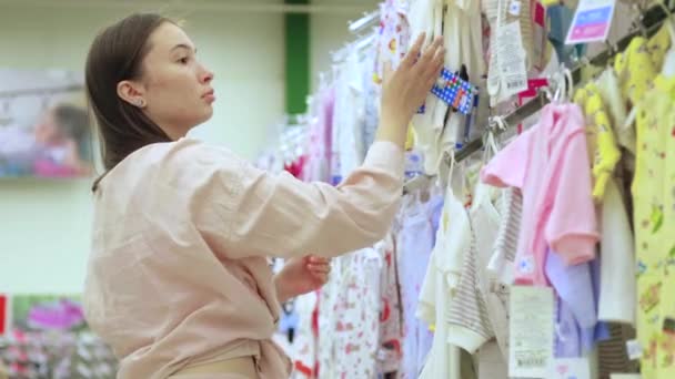 Μια γυναίκα αγοράζει ρούχα για μωρά σε ένα μαγαζί. — Αρχείο Βίντεο