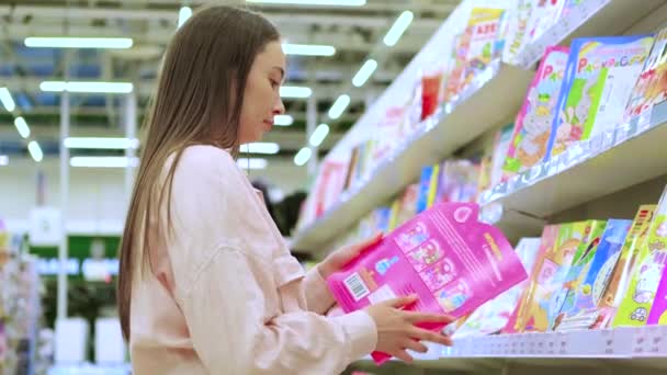 Jongedame koopt een boek voor haar kind in de winkel — Stockvideo