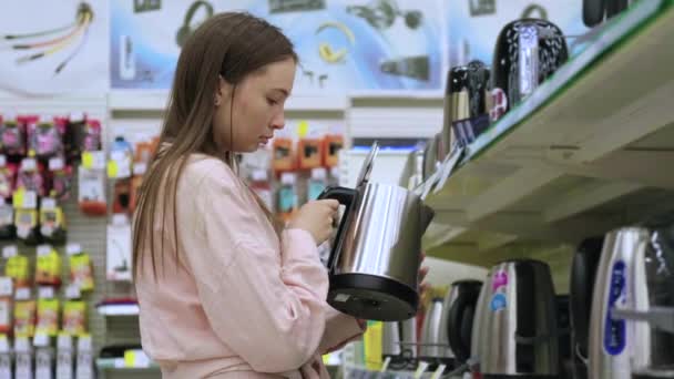 Jonge vrouw koopt een waterkoker in het winkelcentrum — Stockvideo