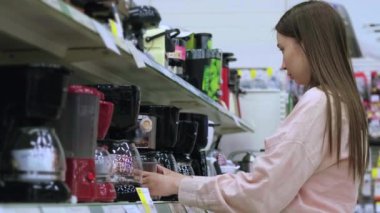 Ev aletleri mağazasından alışveriş yapan kadın kahve makinesini seçiyor.