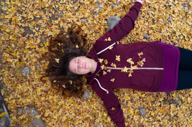 Sarı sonbahar yapraklarında uzanan kadın, gözleri kapalı, sonbahar mevsiminin tadını çıkarıyor.