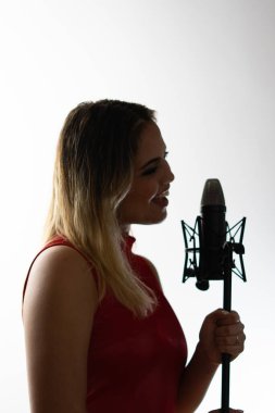 Kayıt stüdyosunda mikrofona şarkı söyleyen genç bir kadının profili.