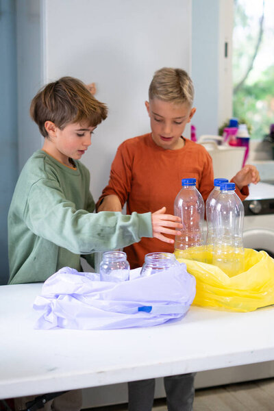 Two young brothers are sorting glass jars and plastic bottles into separate recycling bags in a kitchen, promoting environmental awareness