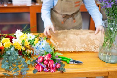 Çiçekçi çiçekçide renkli çiçek buketleri için ambalaj kağıdı hazırlıyor.