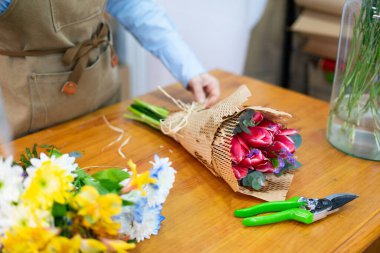 Çiçekçi lale buketi hazırlıyor, çiçekçi, işyeri ve küçük işletme konseptiyle geri dönüşümlü kağıtla sarılıyor.