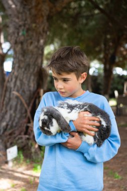 Genç çocuk tavşanını nazikçe dışarıda tutuyor, çocuklar ve hayvanlar arasındaki bağı gösteriyor.