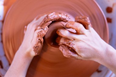 Potter 'ın elleri dönen bir çömlek çarkında kırmızı çamuru ustalıkla şekillendiriyor.