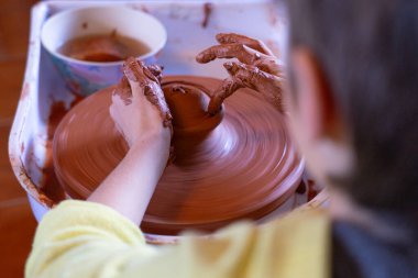 Potter, dönen bir çömlek çarkında kırmızı çamuru dikkatlice şekillendiriyor. Yetenekli elleri kullanarak eşsiz bir gemi yaratıyor.