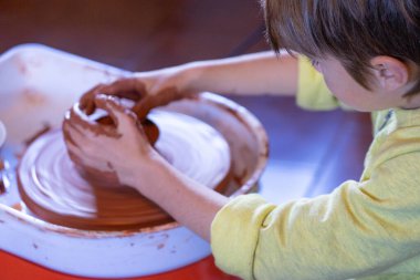 Sanat stüdyosunda çömlek tekeri kullanan genç bir çocuk.