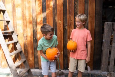 Balkabağı tutan iki mutlu çocuk, kırsal bir duvarın önünde birbirlerine gülümsüyorlar.