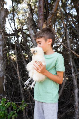 Çocuk dışarıda dikilirken evcil tavuğuna sevgi gösteriyor.