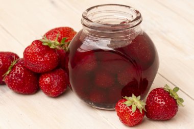 Çilek reçeli Beyaz ahşap zemin üzerinde taze çilek bir kavanoza. Cam kavanoz ile lezzetli çilek lezzetli. Meyveleri küçük kavanoz ile taze ev yapımı çilek reçeli