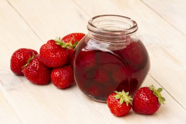 Çilek reçeli Beyaz ahşap zemin üzerinde taze çilek bir kavanoza. Cam kavanoz ile lezzetli çilek lezzetli. Meyveleri küçük kavanoz ile taze ev yapımı çilek reçeli
