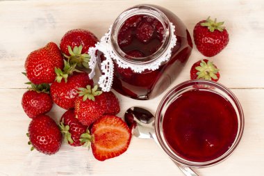 Çilek reçeli Beyaz ahşap zemin üzerinde taze çilek bir kavanoza. Cam kavanoz ve lezzetli çilek lezzetli bir kase. Meyveleri küçük kavanoz ve kaşık ile taze ev yapımı çilek reçeli. en iyi veiw