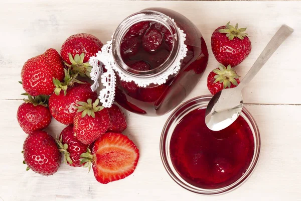 Strawberry jam in a jar with fresh strawberries on white wooden background. Glass jar and bowl with delicious strawberry confiture. Fresh homemade strawberry jam with berries in small jar and spoon. top veiw