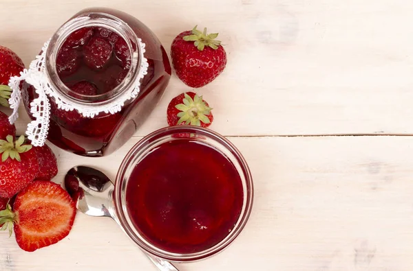 Strawberry jam in a jar with fresh strawberries on white wooden background. Glass jar and bowl with delicious strawberry confiture. Fresh homemade strawberry jam with berries in small jar and spoon. top veiw