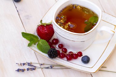 Lavanta ve nane, taze çilek, böğürtlen ve yaban mersini bir beyaz tahta masada bitkisel çay. Berry çay ile taze çilek, böğürtlen. Lavanta bitki çayı ile beyaz porselen fincan