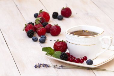 Lavanta ve nane, taze çilek, böğürtlen ve yaban mersini bir beyaz tahta masada bitkisel çay. Berry çay ile taze çilek, böğürtlen. Lavanta bitki çayı ile beyaz porselen fincan