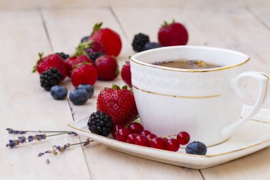 Lavanta ve nane, taze çilek, böğürtlen ve yaban mersini bir beyaz tahta masada bitkisel çay. Berry çay ile taze çilek, böğürtlen. Lavanta bitki çayı ile beyaz porselen fincan