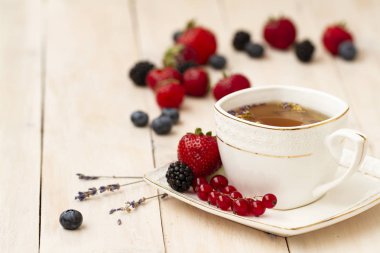 Lavanta ve nane, taze çilek, böğürtlen ve yaban mersini bir beyaz tahta masada bitkisel çay. Berry çay ile taze çilek, böğürtlen. Lavanta bitki çayı ile beyaz porselen fincan