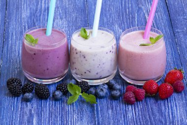 Ahududu, çilek, böğürtlen, blueberry smoothie mavi ahşap zemin üzerinde. taze çilek ile milkshake. sağlıklı kahvaltı. meyve yüzlü malzemelerle. iyi olmak ve ağırlık loos kavramı
