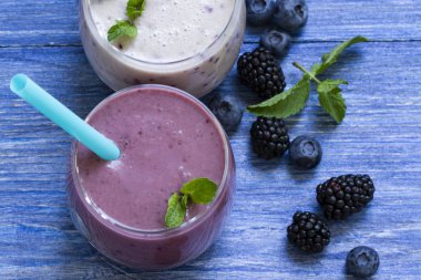 yaban mersini ve blackberry güler yüzlü mavi ahşap zemin üzerinde. taze çilek ile milkshake. sağlıklı kahvaltı. meyve yüzlü malzemelerle. iyi olmak ve ağırlık loos kavramı. üstten görünüm