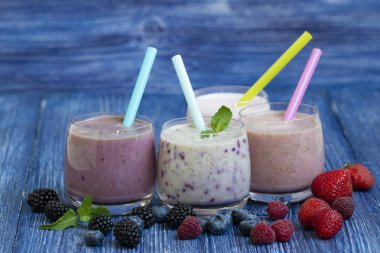 Ahududu, çilek, böğürtlen, blueberry smoothie mavi ahşap zemin üzerinde. taze çilek ile milkshake. sağlıklı kahvaltı. meyve yüzlü malzemelerle. iyi olmak ve ağırlık loos kavramı