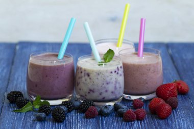 Ahududu, çilek, böğürtlen, blueberry smoothie mavi ahşap zemin üzerinde. taze çilek ile milkshake. sağlıklı kahvaltı. meyve yüzlü malzemelerle. iyi olmak ve ağırlık loos kavramı