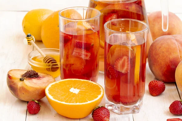 Summer refreshing drinks. Fruit, berry cocktail. compote with peach, strawberry, orange, hioney. Cold fruit and berry tea in faceted highball, healthy drink. Dietary detox drink on light background. — Stock Photo, Image