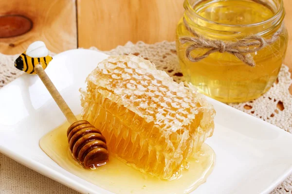 Bal tarak parçası. Bal kaşığı ve ahşap masada bal kavanozu ile ballı dilim. balmumu ve sıvı doğal sarı bal ile petek parçası. Rustik. Organik doğal malzemeler konsepti ile arı ürünleri