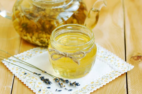 Miel en frasco de vidrio con lavanda y té de hierbas en tetera de vidrio en primer plano servilleta de lino de encaje. miel amarilla natural líquida. Un estilete rústico. productos de abeja por concepto de ingredientes naturales orgánicos — Foto de Stock