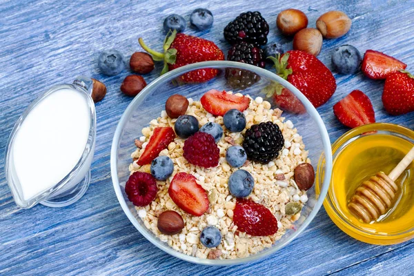 healthy muesli with raspberry, blueberry, strawberry, BlackBerry, hazelnut, milk and honey on blue wooden rustic table. homemade muesli or granola, fresh berries. Top view. Healthy diet.