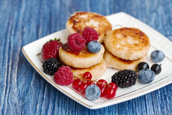 Cottage cheese pancakes, syrniki, curd fritters with fresh berries on blue background. healthy delicacy breakfast or lunch. Homemade cheese pancakes with fresh berries. closeup, selective focus.